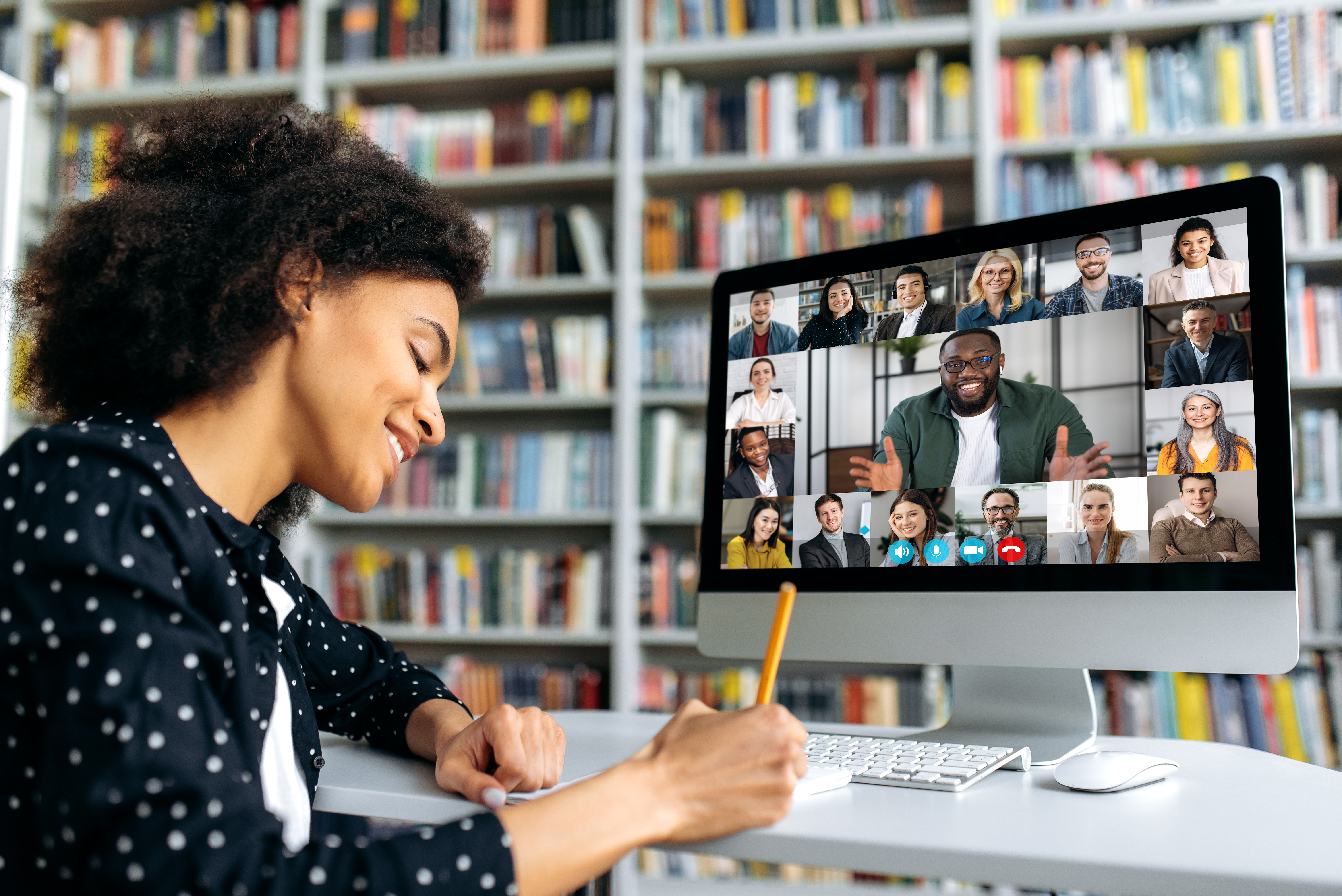 A Behaviorly student takes notes while attending a group class over video in a room full of books.