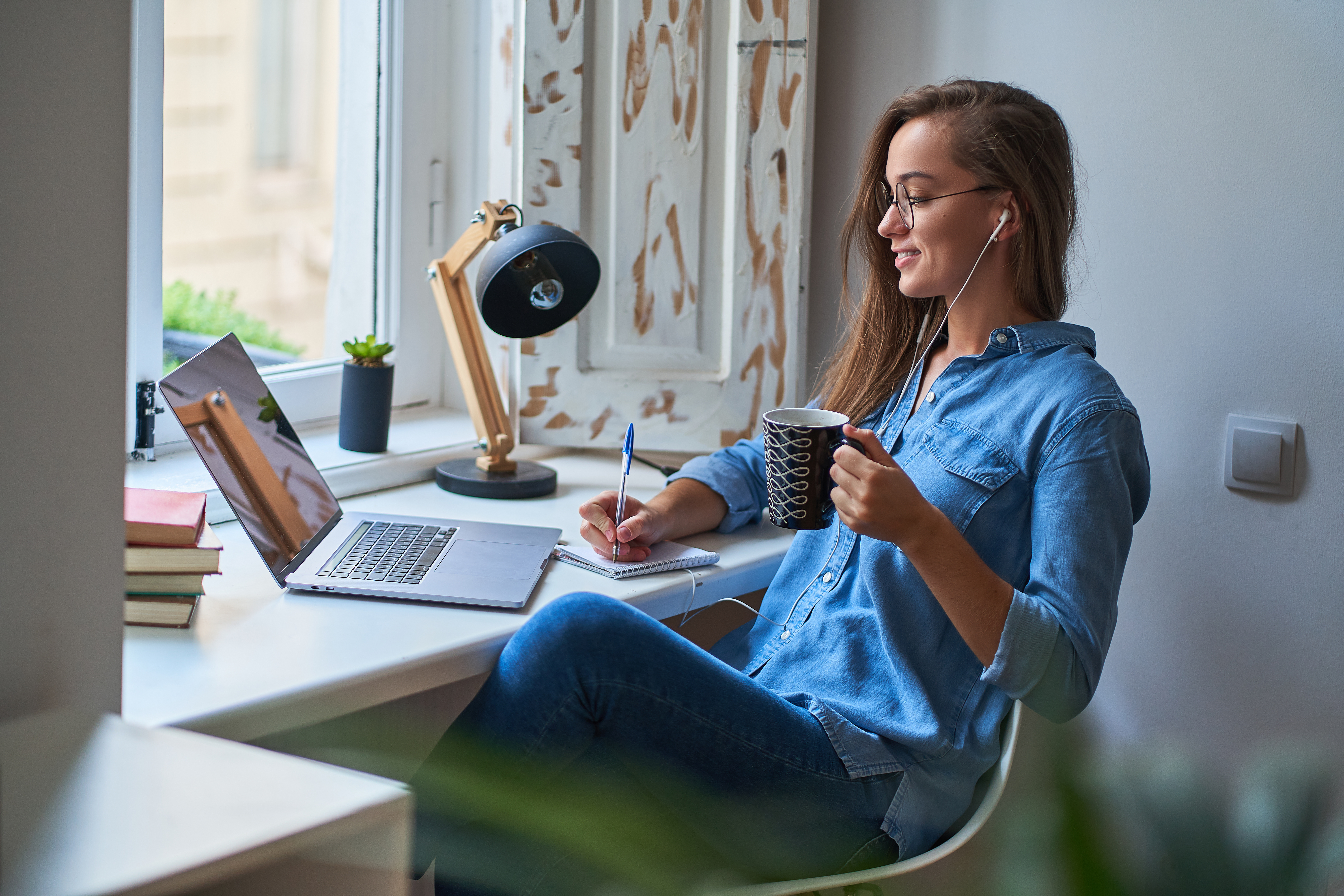 An RBT takes notes from a video on her laptop while sipping coffee and wearing headphones in her office.