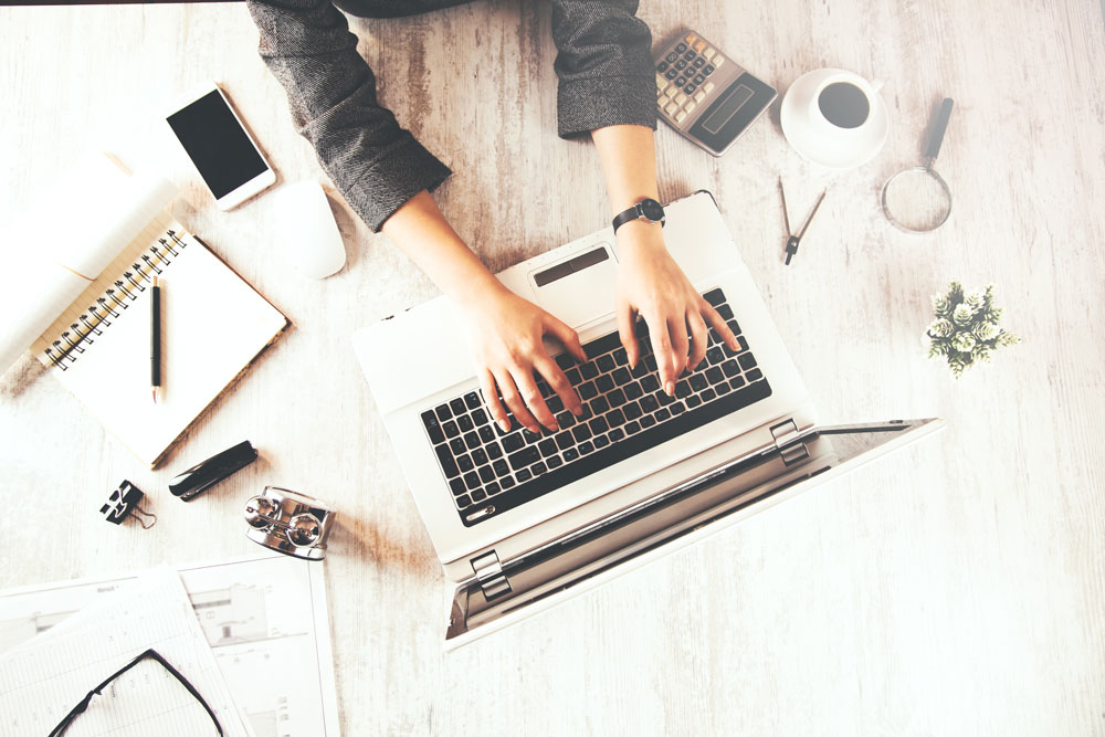 An image of an RBT typing on their laptop with their cell phone and notepad next to them.