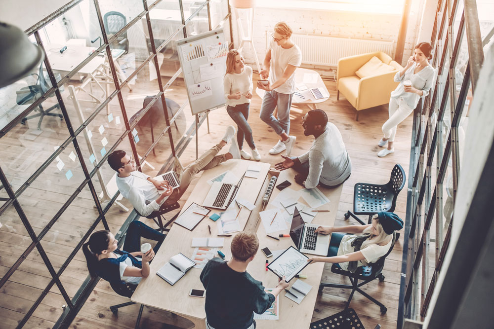 Eight young RBTs gather in a bright, modern, airy office, with laptops and notebooks open to work tasks.