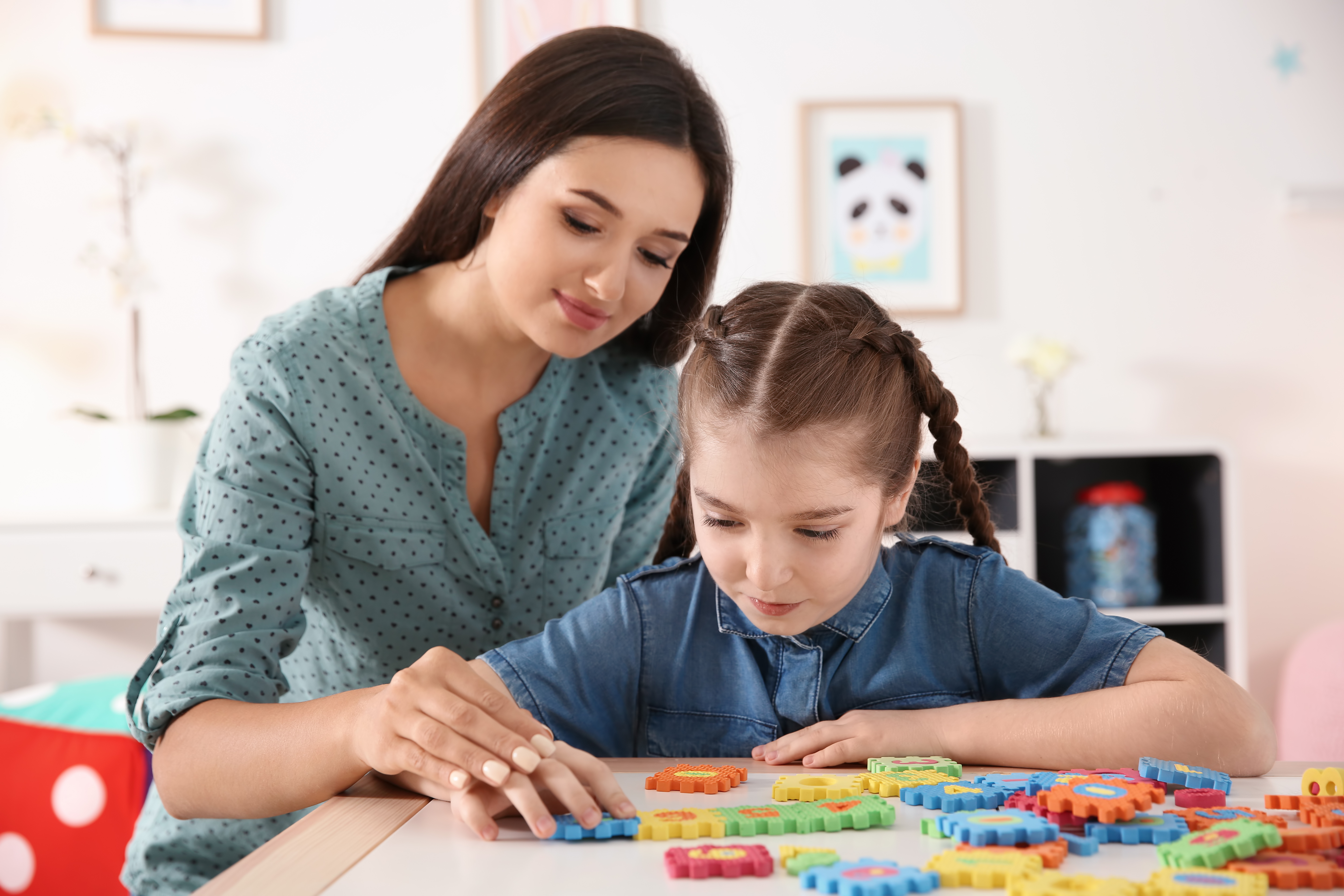 A student works on a colorful puzzle as her caring RBT looks on and assists.