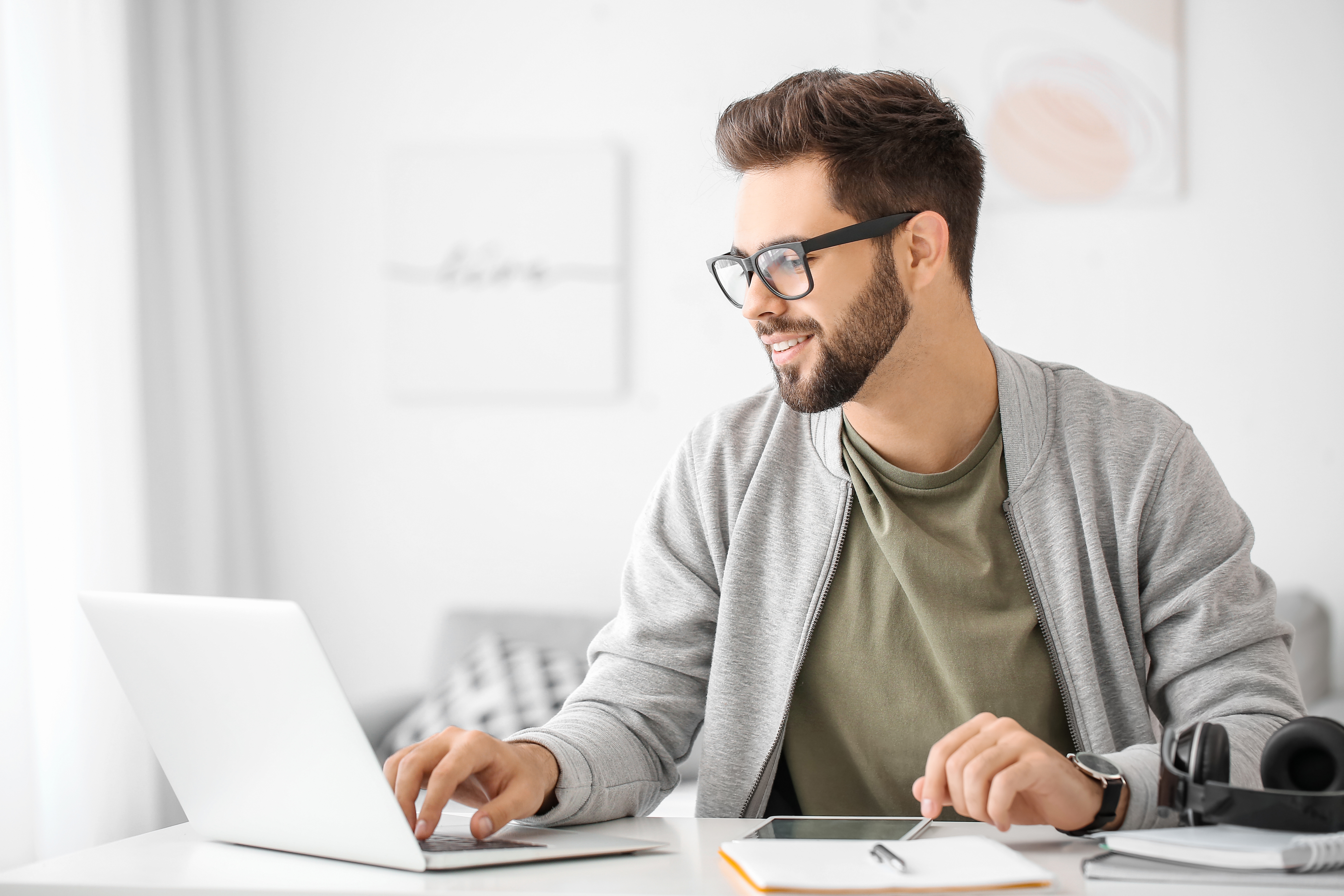 A clean-cut RBT in glasses completes his certification exam on a laptop with his notes nearby.