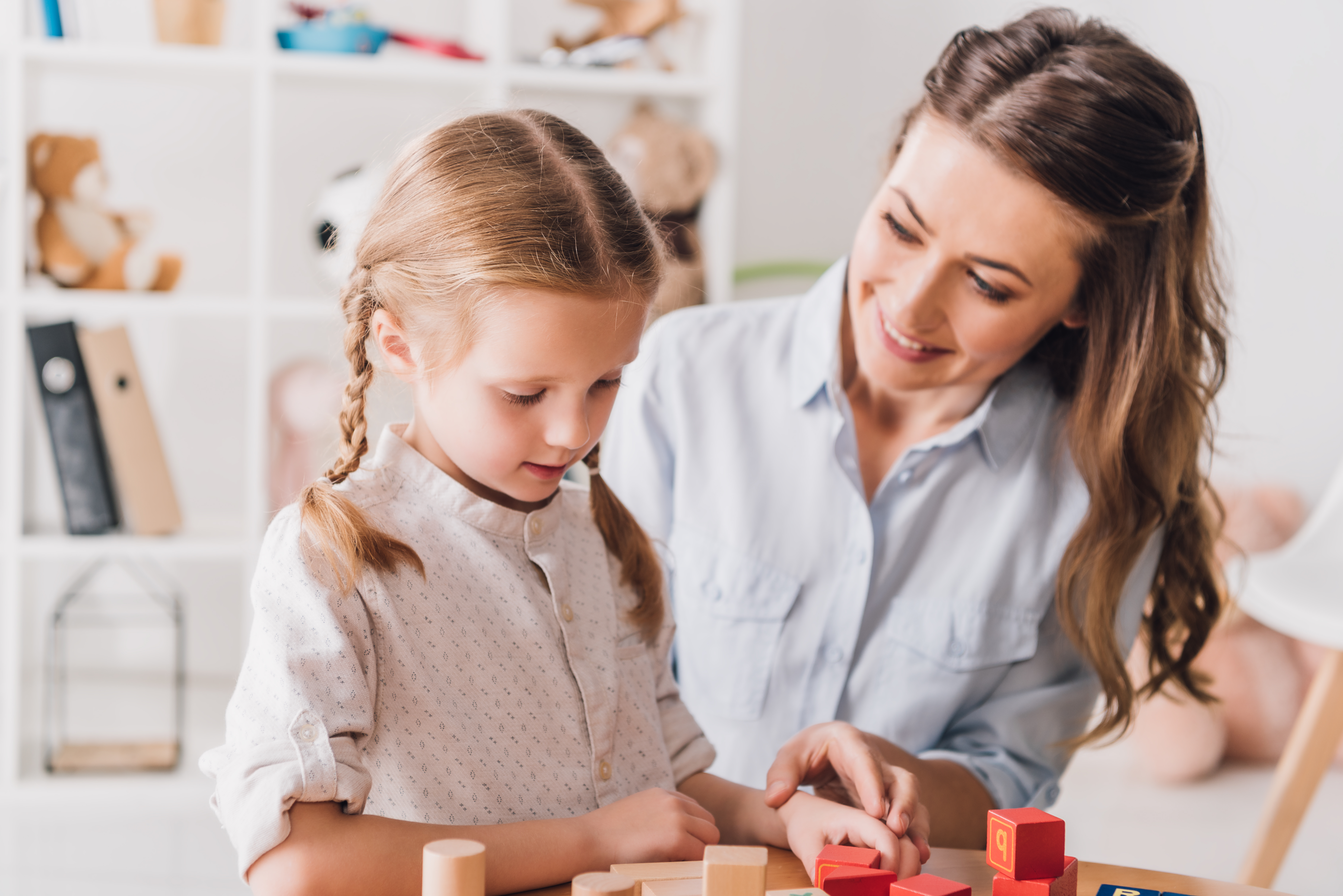 A professional looking behavior specialist helps a curious student assemble wooden blocks.